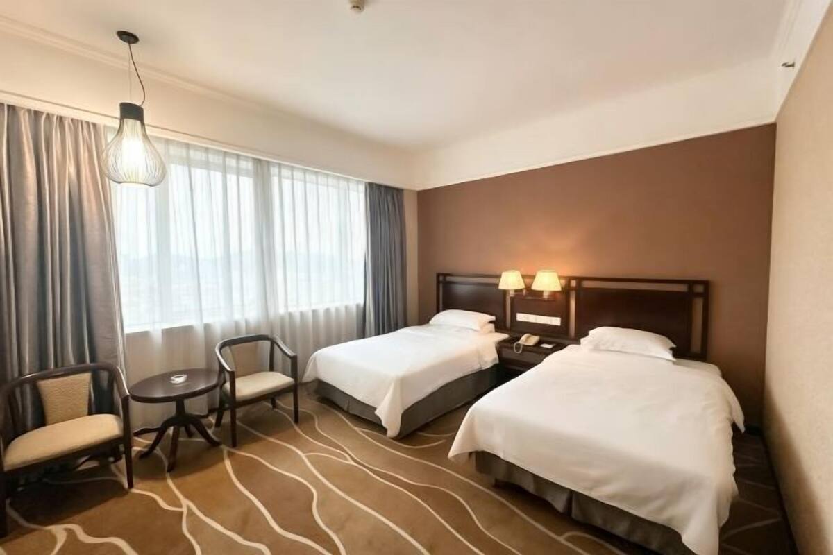 A hotel room with two beds, a desk, a chair, and a lamp.