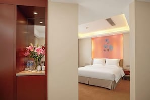 A hotel room with a bed, a nightstand, a vase of flowers, and a wall-mounted light fixture. - Celeste Palace Hotel (Jiangmen)