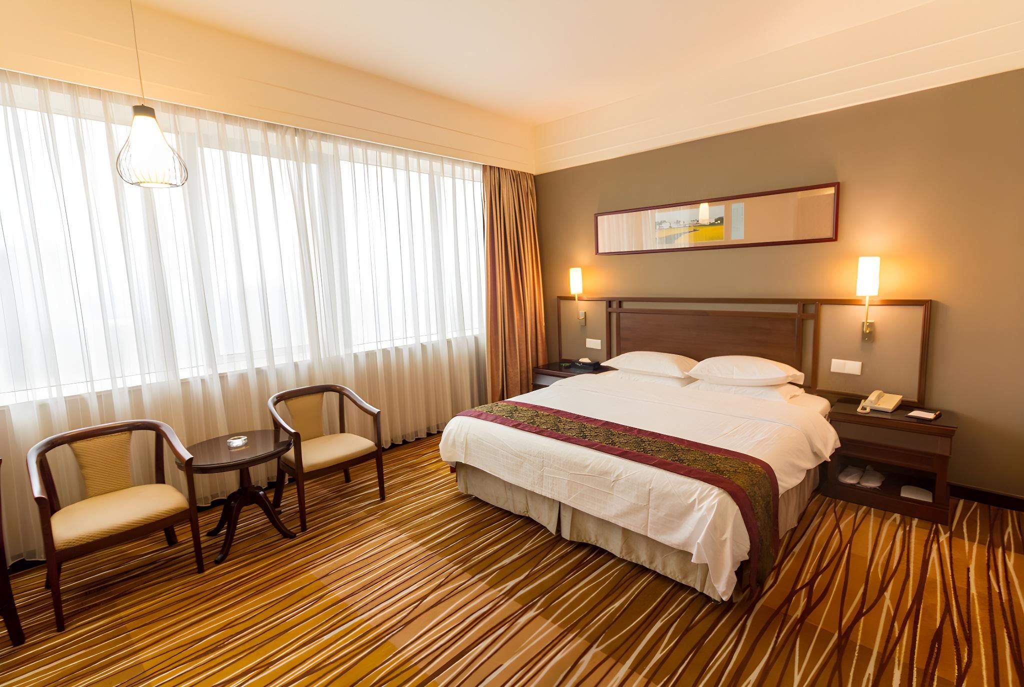 A hotel room with a bed, two chairs, a nightstand, and a lamp.