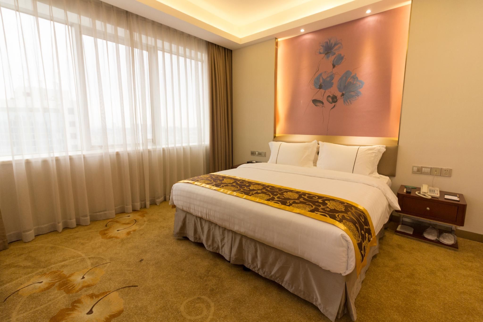 A hotel room with a bed, a nightstand, a wall-mounted telephone, and a window with curtains.