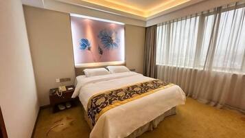 A hotel room with a large bed, a bedside table, a wall-mounted TV, and a window with curtains.