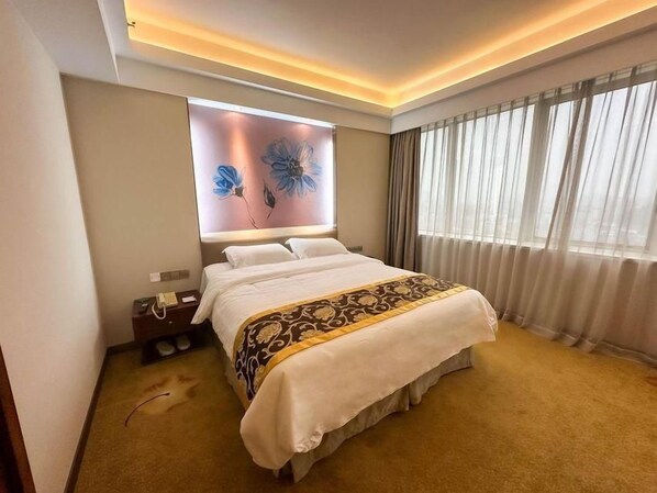 Une chambre d’hôtel avec un grand lit, une table de chevet, un téléviseur fixé au mur et une fenêtre avec des rideaux.