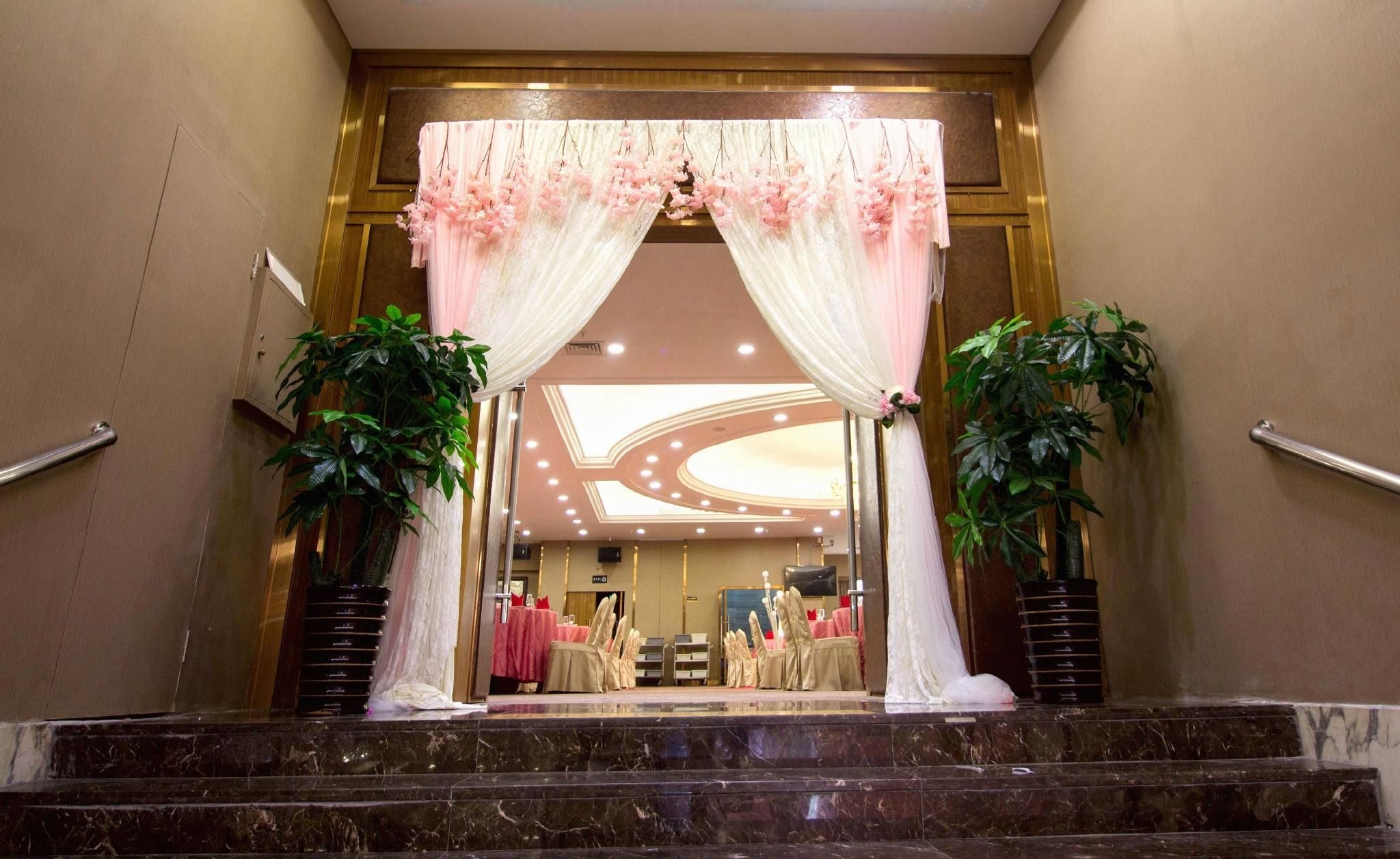 A hotel entrance with a marble staircase, a reception desk, and a seating area with tables and chairs.
