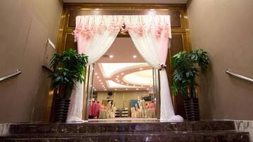 A hotel entrance with a marble staircase, a reception desk, and a seating area with tables and chairs.