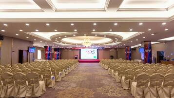 A conference room with rows of chairs, a stage with a screen, and a chandelier.