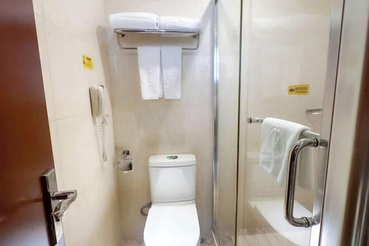 A small, compact bathroom with a toilet, a glass shower enclosure, a towel rack, and a hand dryer.