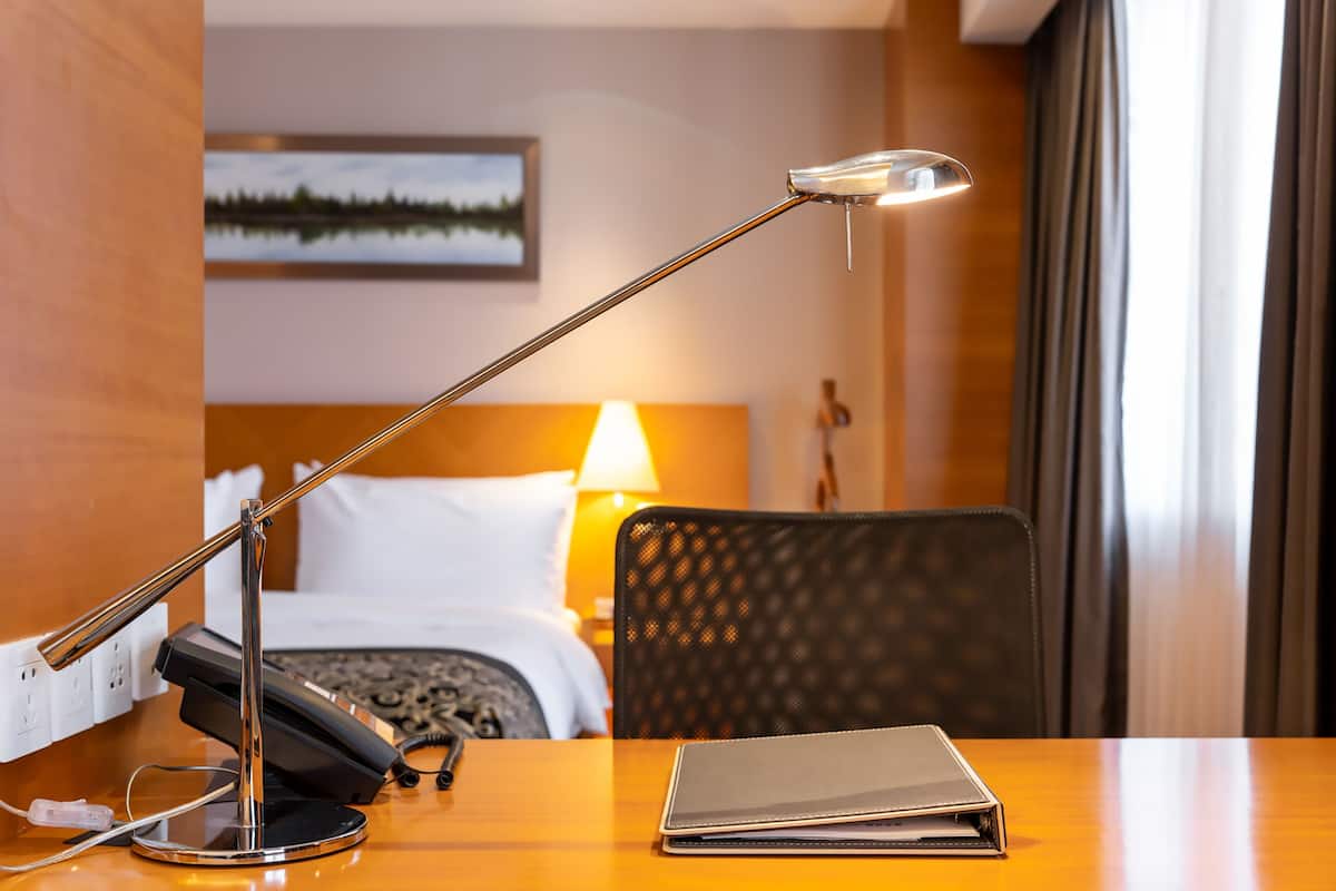 Une chambre d’hôtel équipée d’un bureau, d’une lampe, d’un téléphone, d’un ordinateur portable, d’un lit et d’un tableau au mur.
