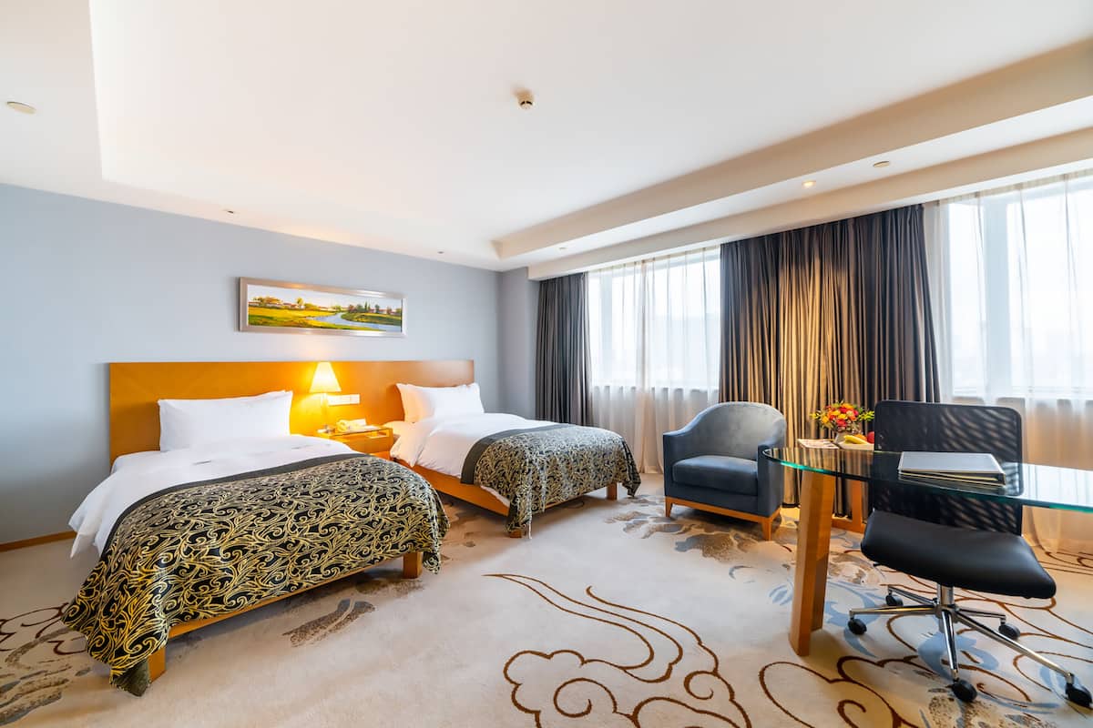 Une chambre d’hôtel avec deux lits, un bureau avec une chaise, une lampe et un tableau au mur.