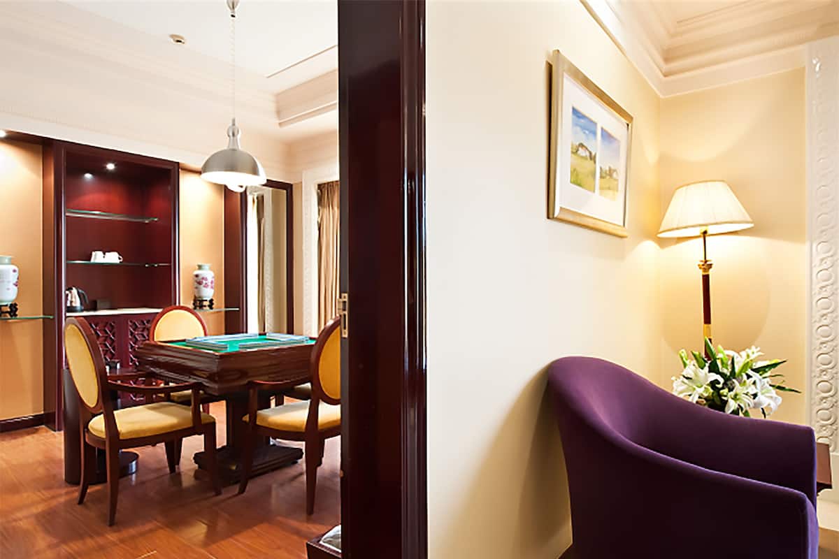 Une chambre d’hôtel avec une table à manger en bois, des chaises, un billard, un fauteuil violet, une lampe et un tableau encadré au mur.