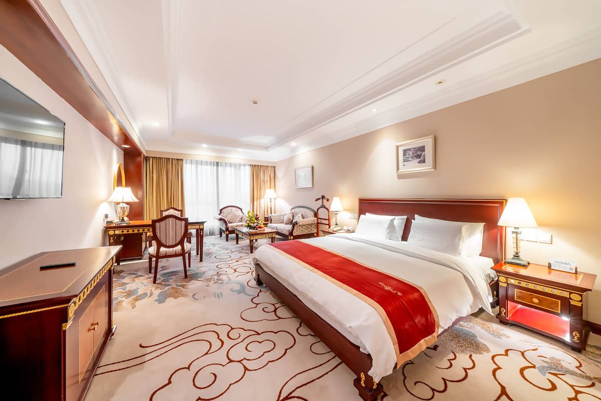Une chambre d’hôtel avec un grand lit, un bureau, deux chaises, une petite table et une table de chevet avec une lampe.