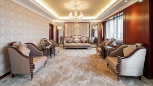Une chambre luxueuse avec un tapis à motifs, un grand canapé, deux fauteuils et un lustre.