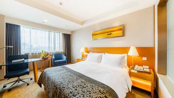Ein Hotelzimmer mit einem großen Bett, einem Schreibtisch mit Stuhl, einem kleinen Tisch mit Blumen und Blick auf die Stadt durch das Fenster.