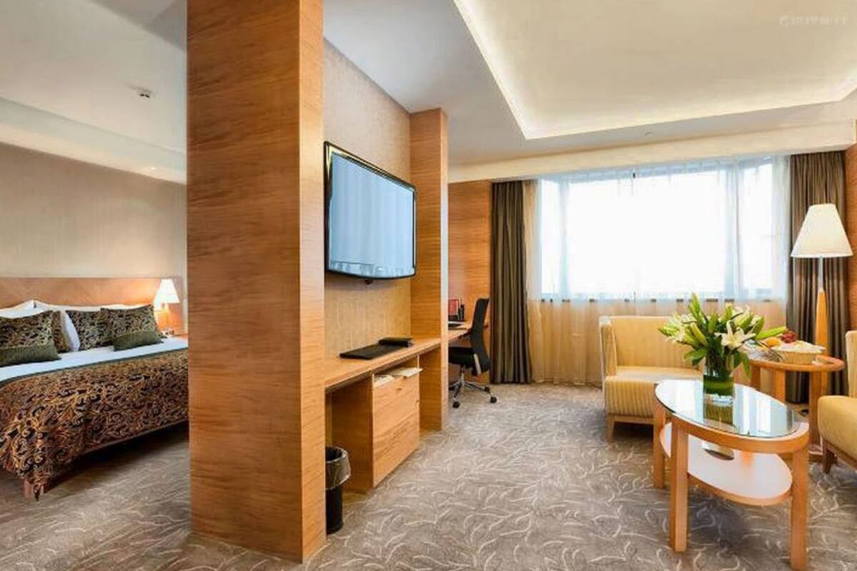 Une chambre d’hôtel comprenant un lit, un bureau, une télévision, un canapé et une petite table sur laquelle est posé un vase de fleurs.