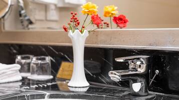 Un tocador de baño con un jarrón blanco con flores amarillas y rojas, una encimera de mármol negro y un grifo de cromo.