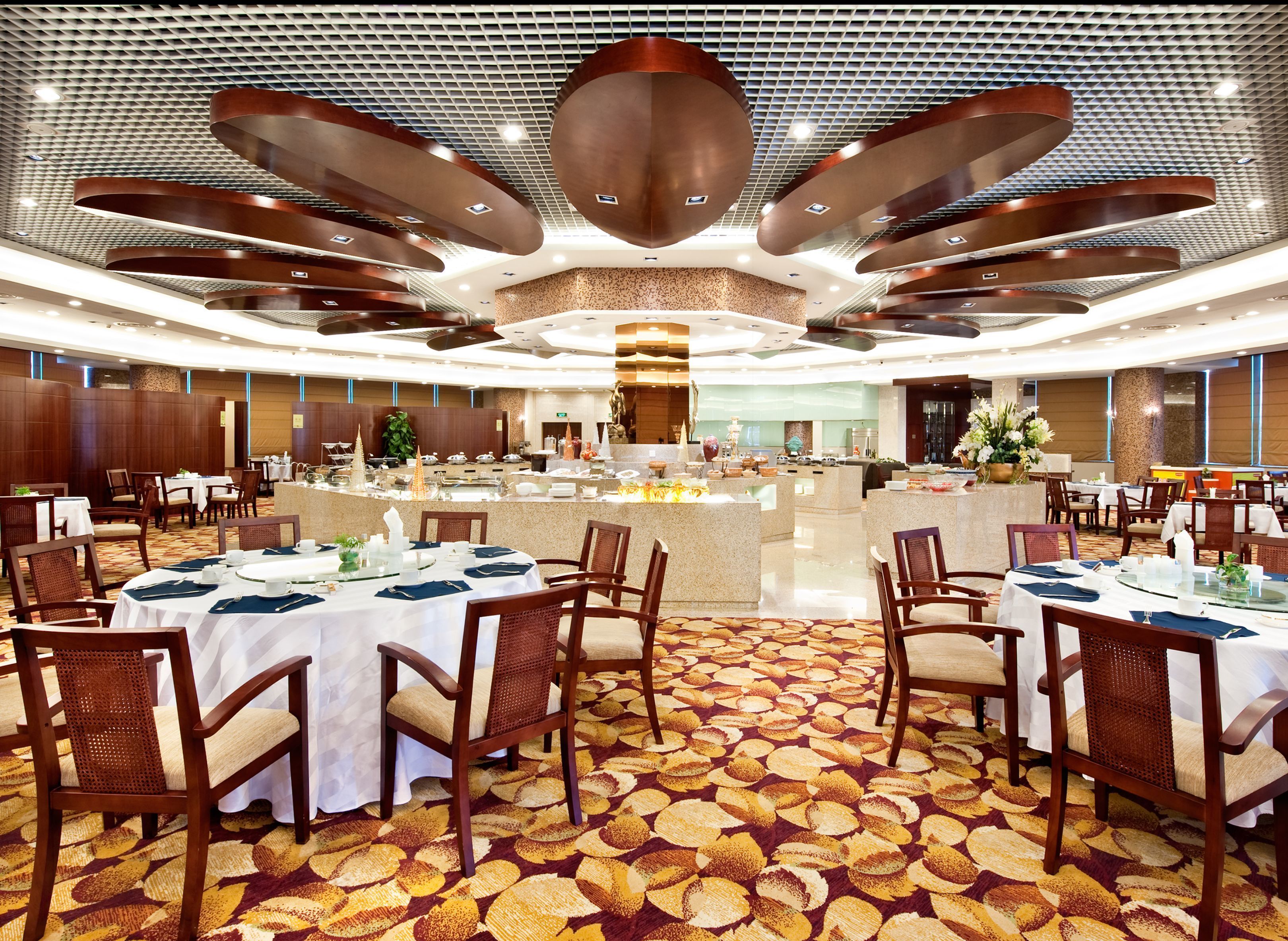 A spacious banquet hall with round tables, chairs, and a central buffet area.