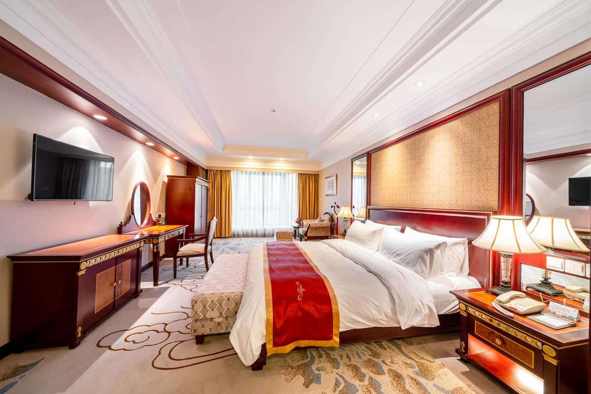 Une chambre d’hôtel avec un grand lit, un bureau avec un miroir, une commode et un téléviseur fixé au mur.