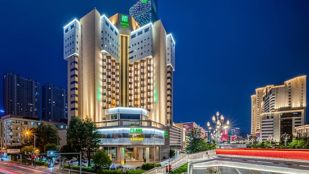 A multi-story hotel with a prominent Holiday Inn sign, surrounded by other buildings and a busy road with light trails. - Holiday Inn Kunming City Centre by IHG (Kunming)