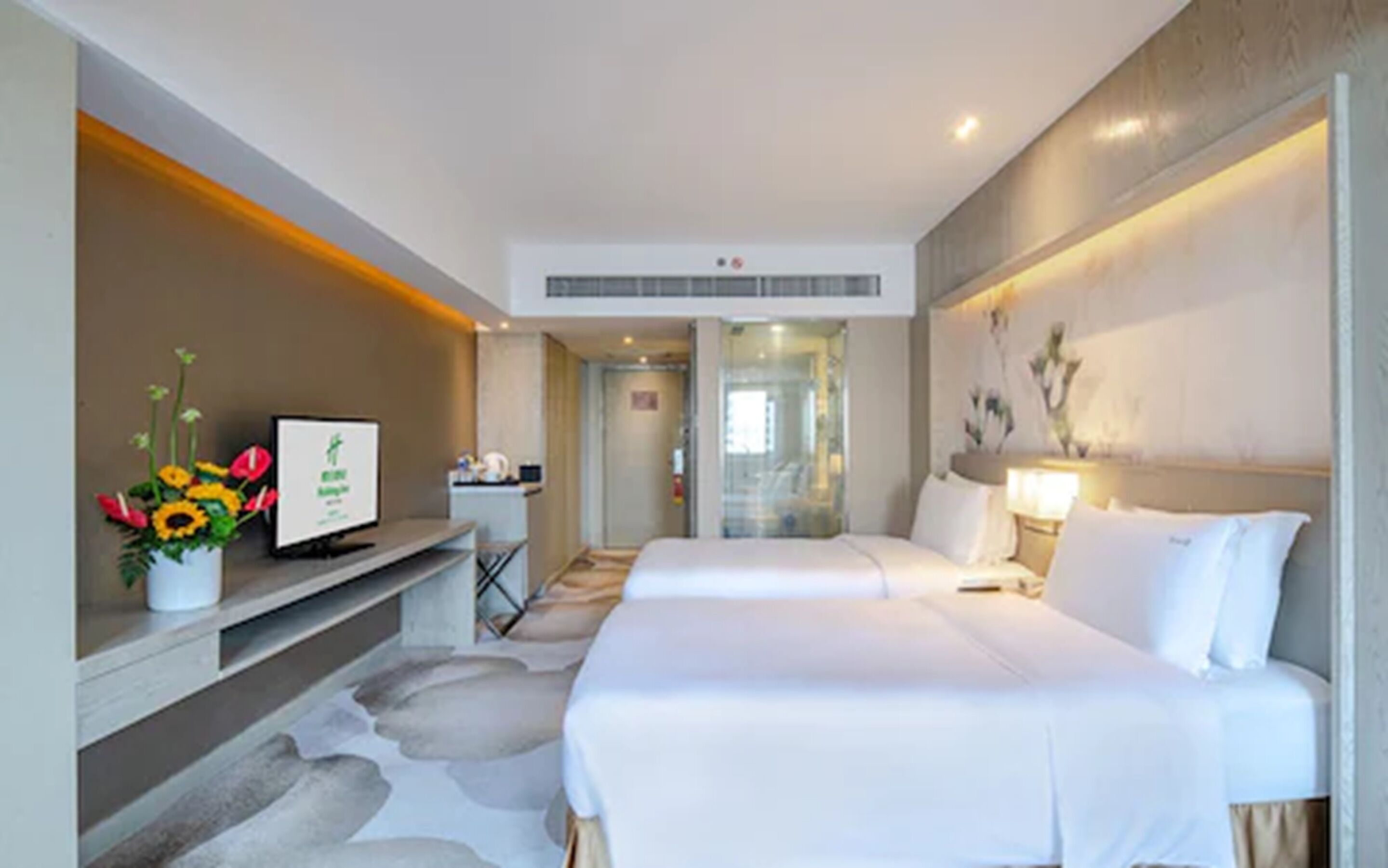 Ein Hotelzimmer mit Bett, Schreibtisch, Fernseher und einer Zimmerpflanze.