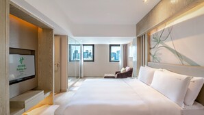 A hotel room with a large bed, a TV on the left, and a city view through the windows. - Holiday Inn Kunming City Centre by IHG (Kunming)