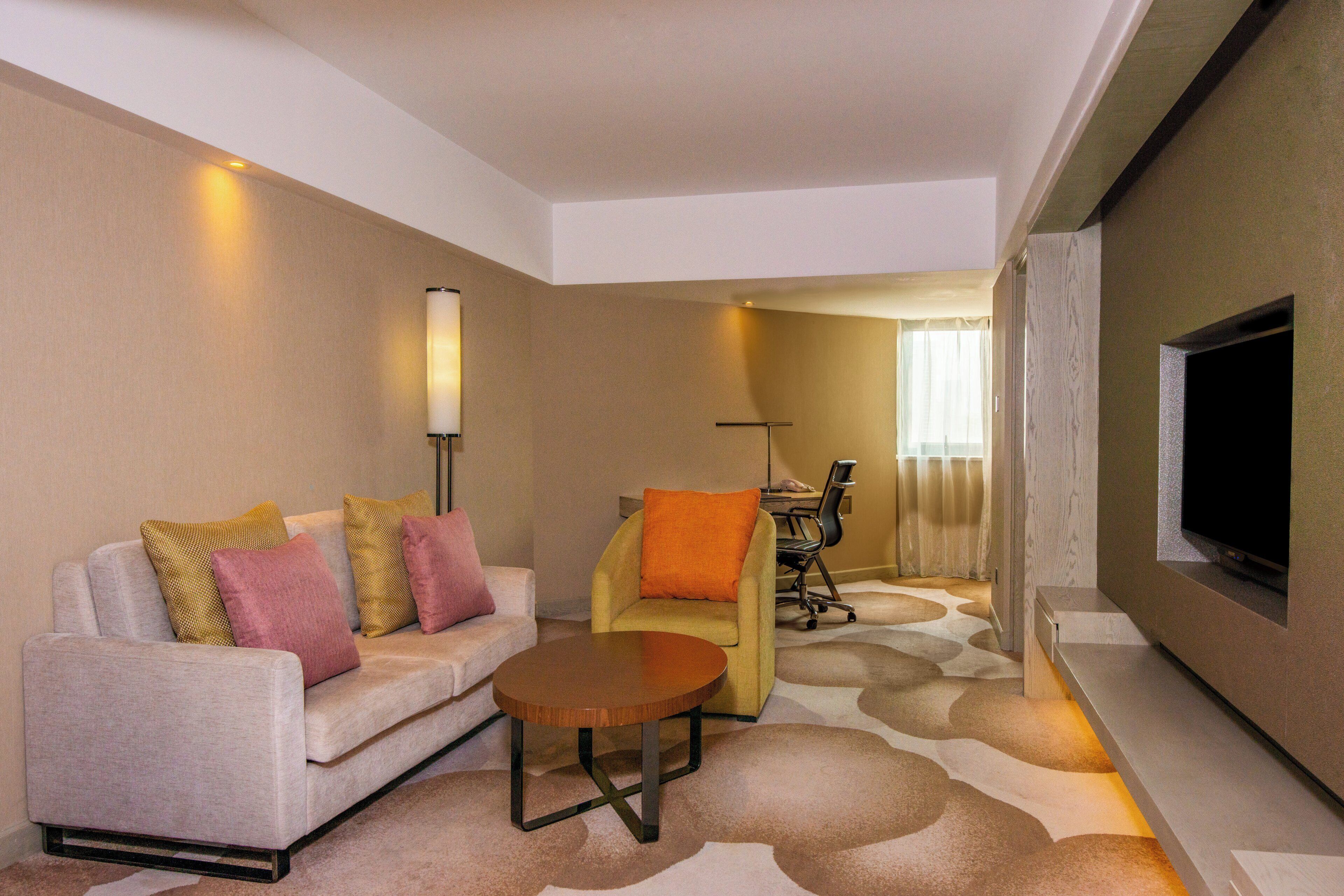 Habitación de hotel con sofá, sillón, mesita y televisor montado en la pared.