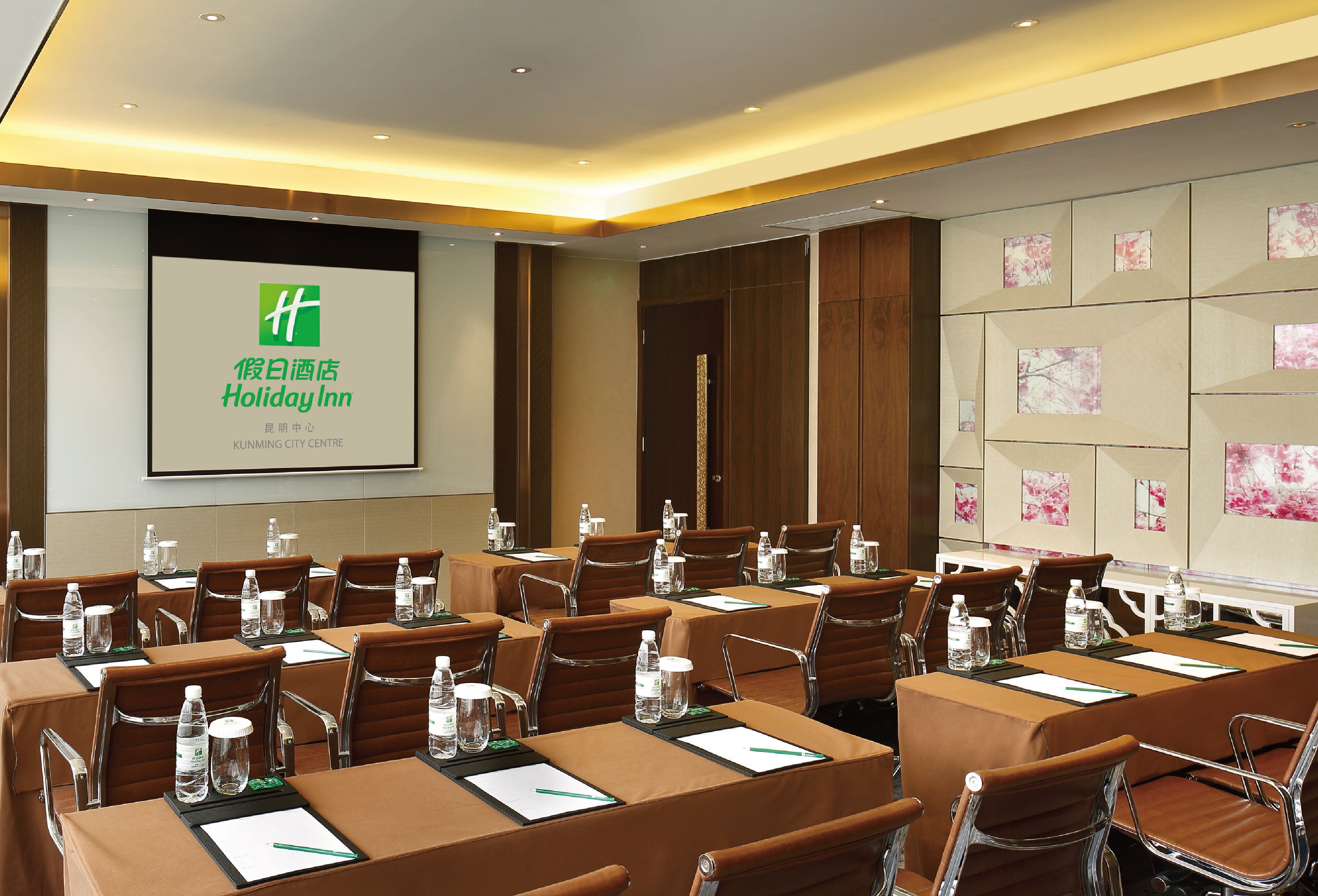 Una sala de conferencias con mesas, sillas y una pantalla de proyección que muestra la marca del hotel.