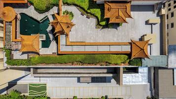 An aerial view of a hotel with a rooftop pool, sun loungers, and a green lawn area.
