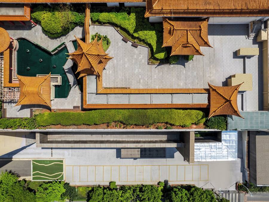 An aerial view of a hotel with a rooftop pool, sun loungers, and a green lawn area.