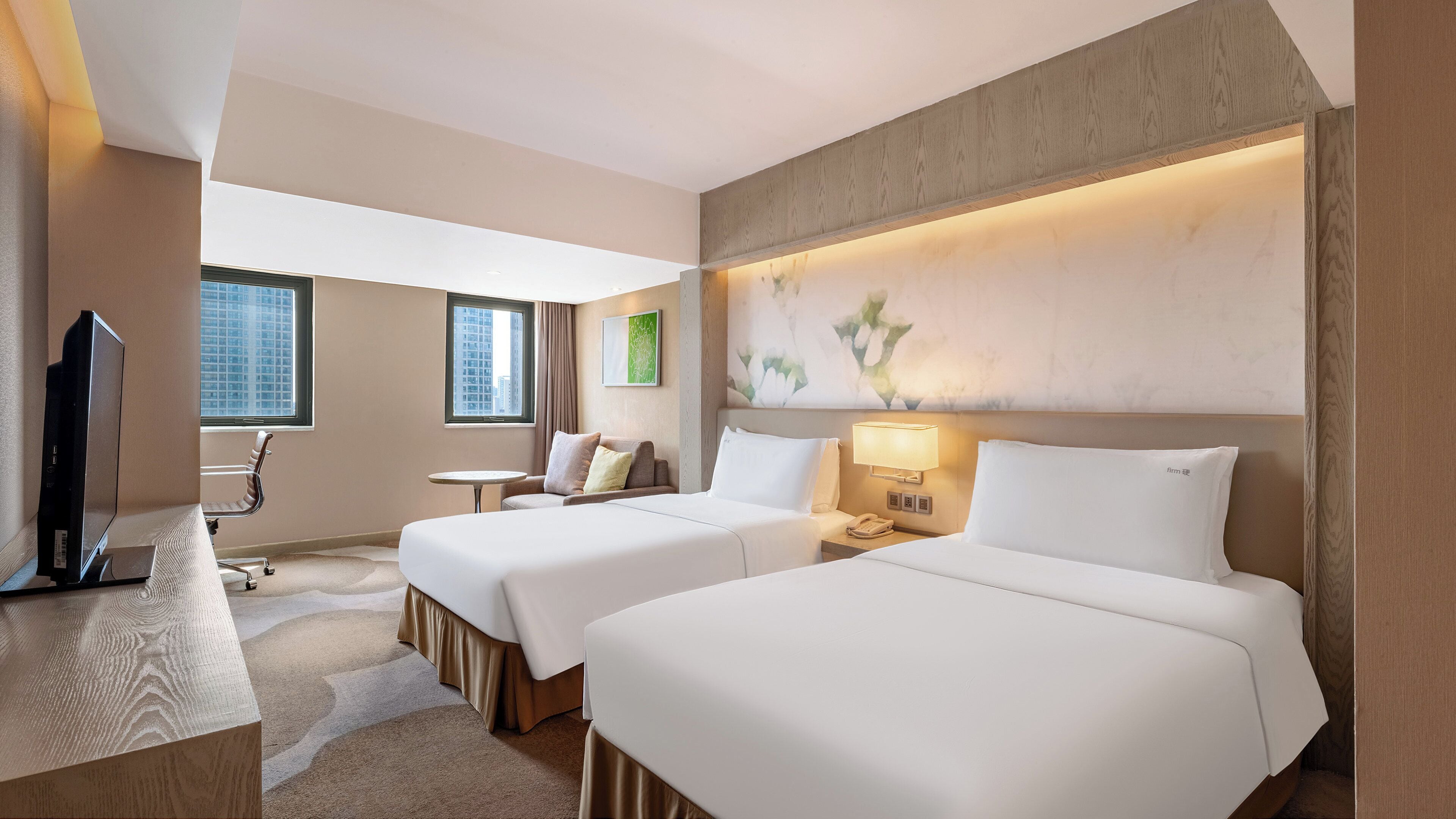 Ein Hotelzimmer mit zwei Betten, einem Schreibtisch, einem Fernseher und Blick auf ein Gebäude.