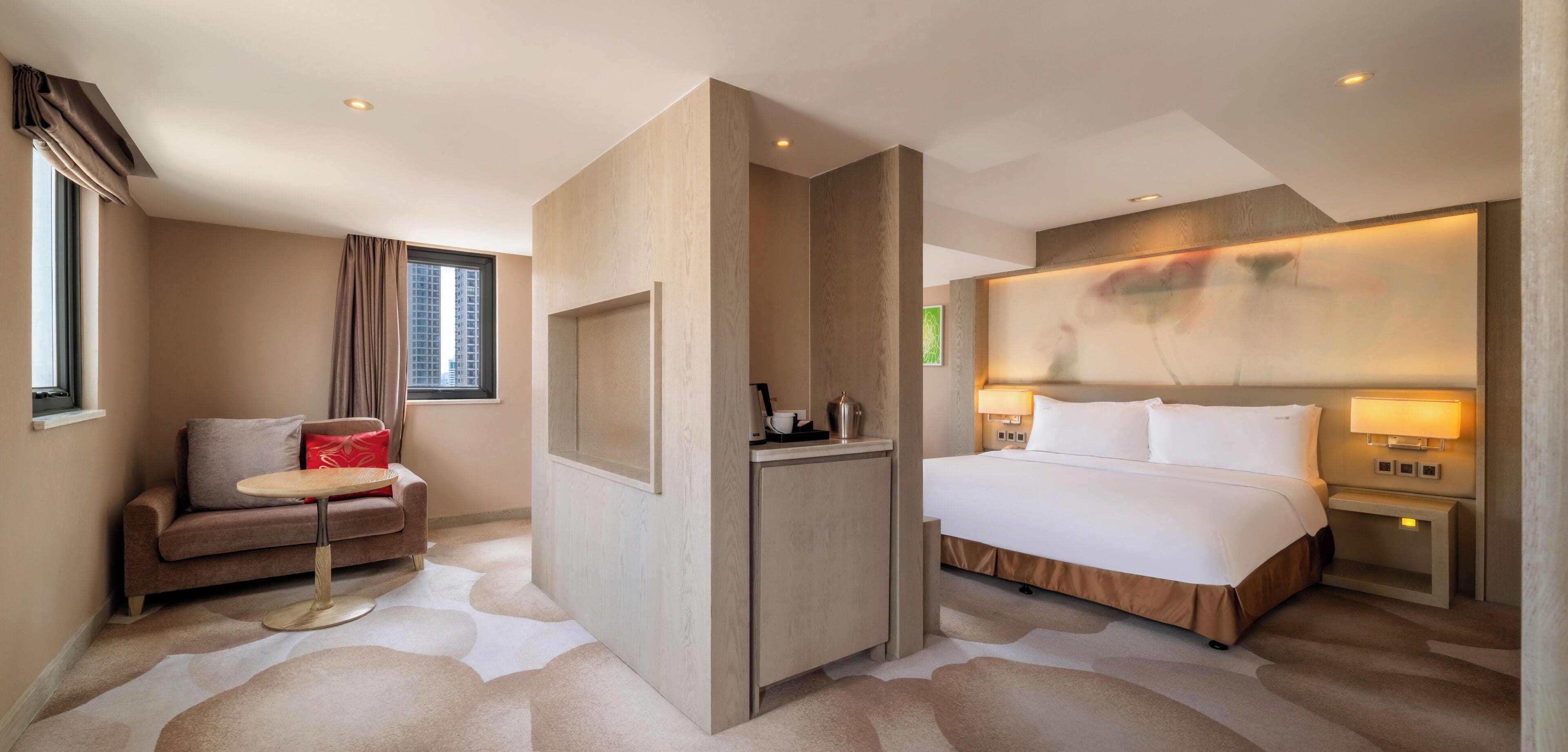 A hotel room with a bed, a sofa, a small table, a nightstand, and a wall-mounted TV.