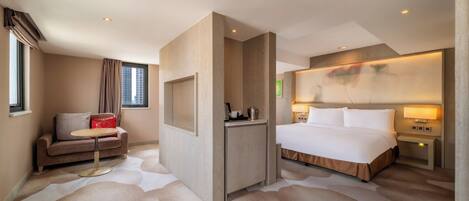A hotel room with a bed, a sofa, a small table, a nightstand, and a wall-mounted TV.