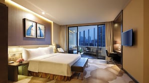 A hotel room with a bed, bedside table, lamp, artwork, and a TV. - Holiday Inn Kunming City Centre by IHG (Kunming)