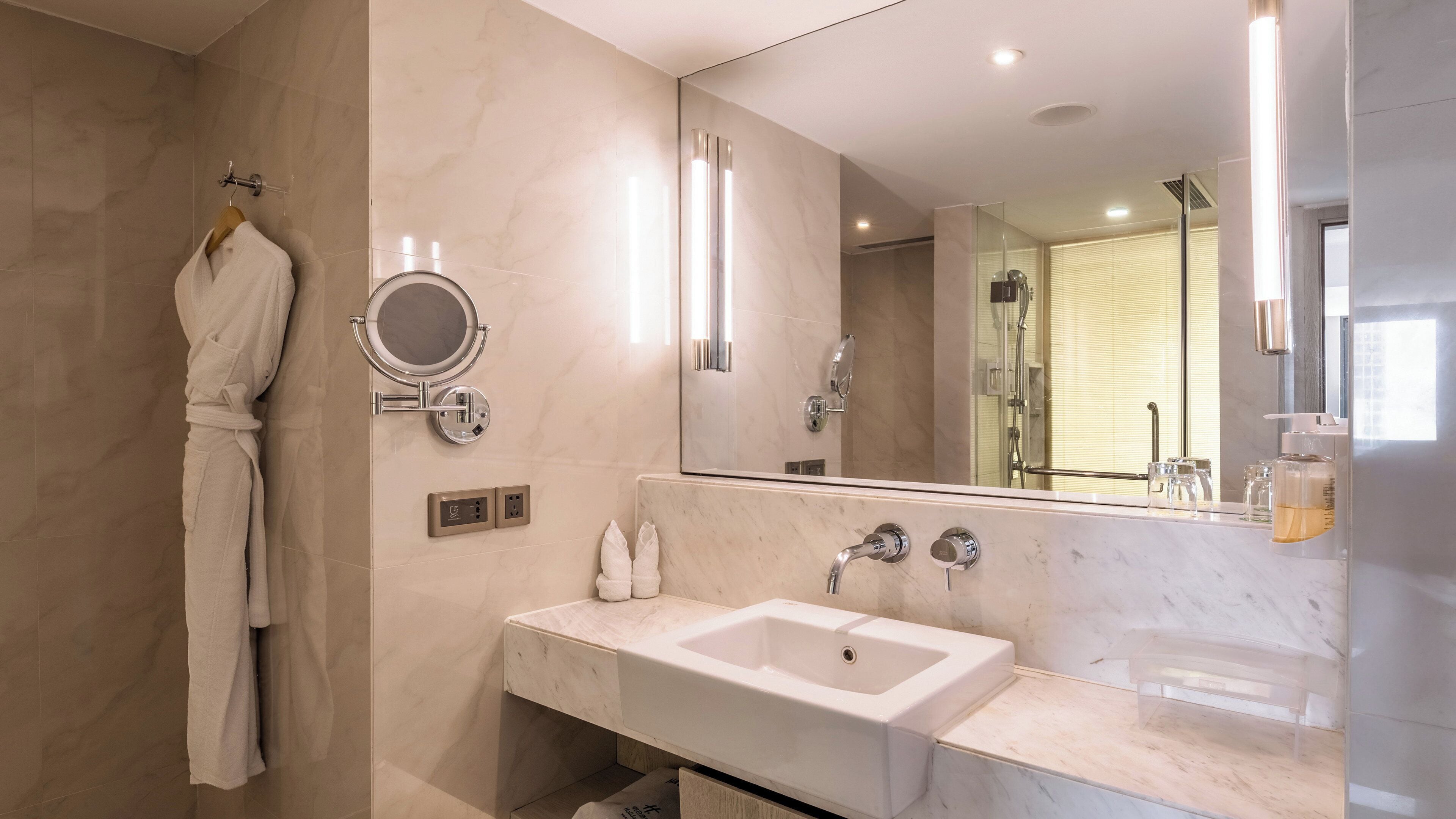 A modern bathroom with a marble sink, a mirror, and a robe hanging on a rack.