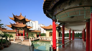 Een traditionele Chinese architectuurconstructie met meerdere verdiepingen en rode pilaren, een klein vijvertje en een helderblauwe lucht.