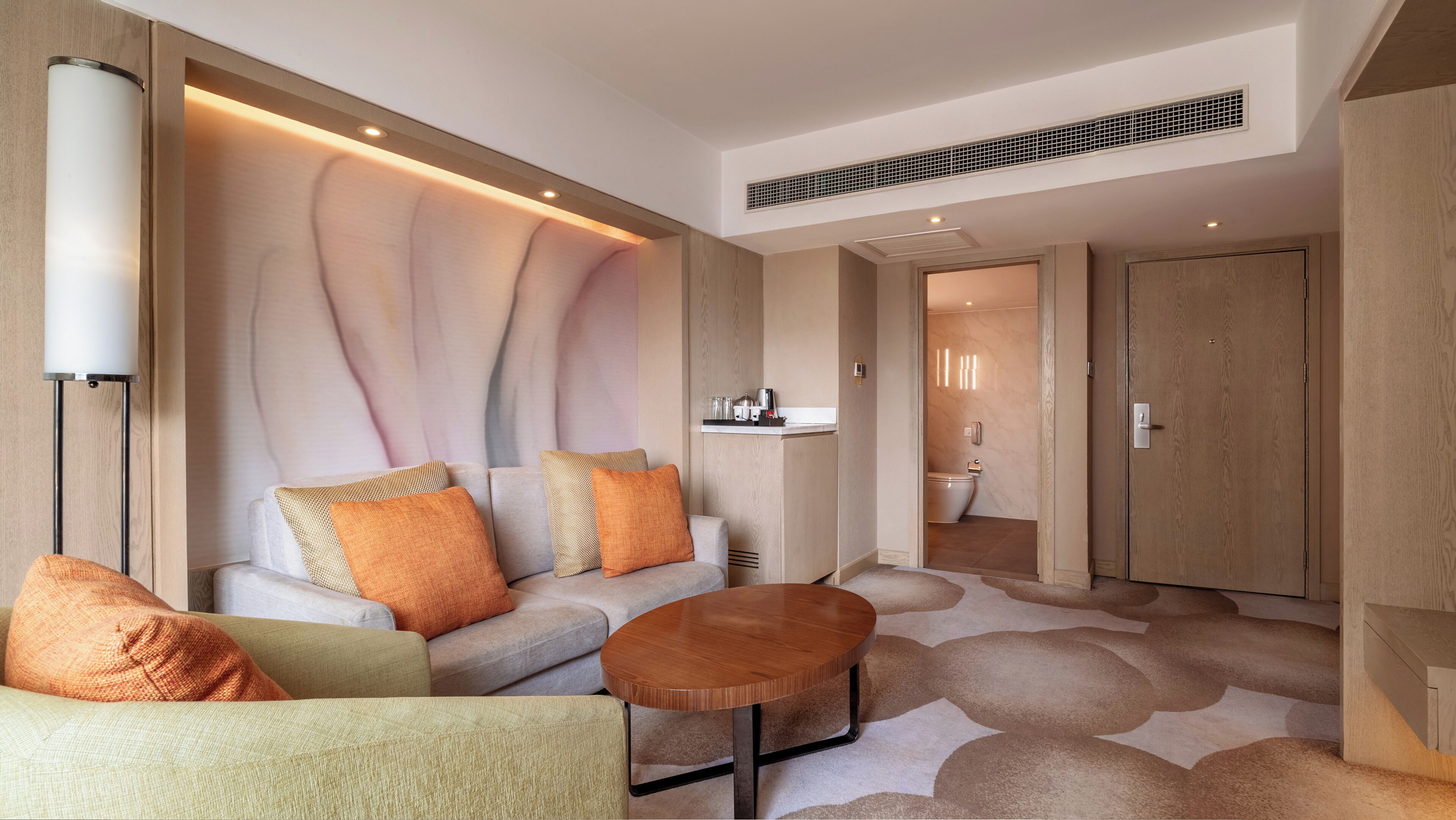 A modern hotel room with a sofa, coffee table, and a small kitchenette area.