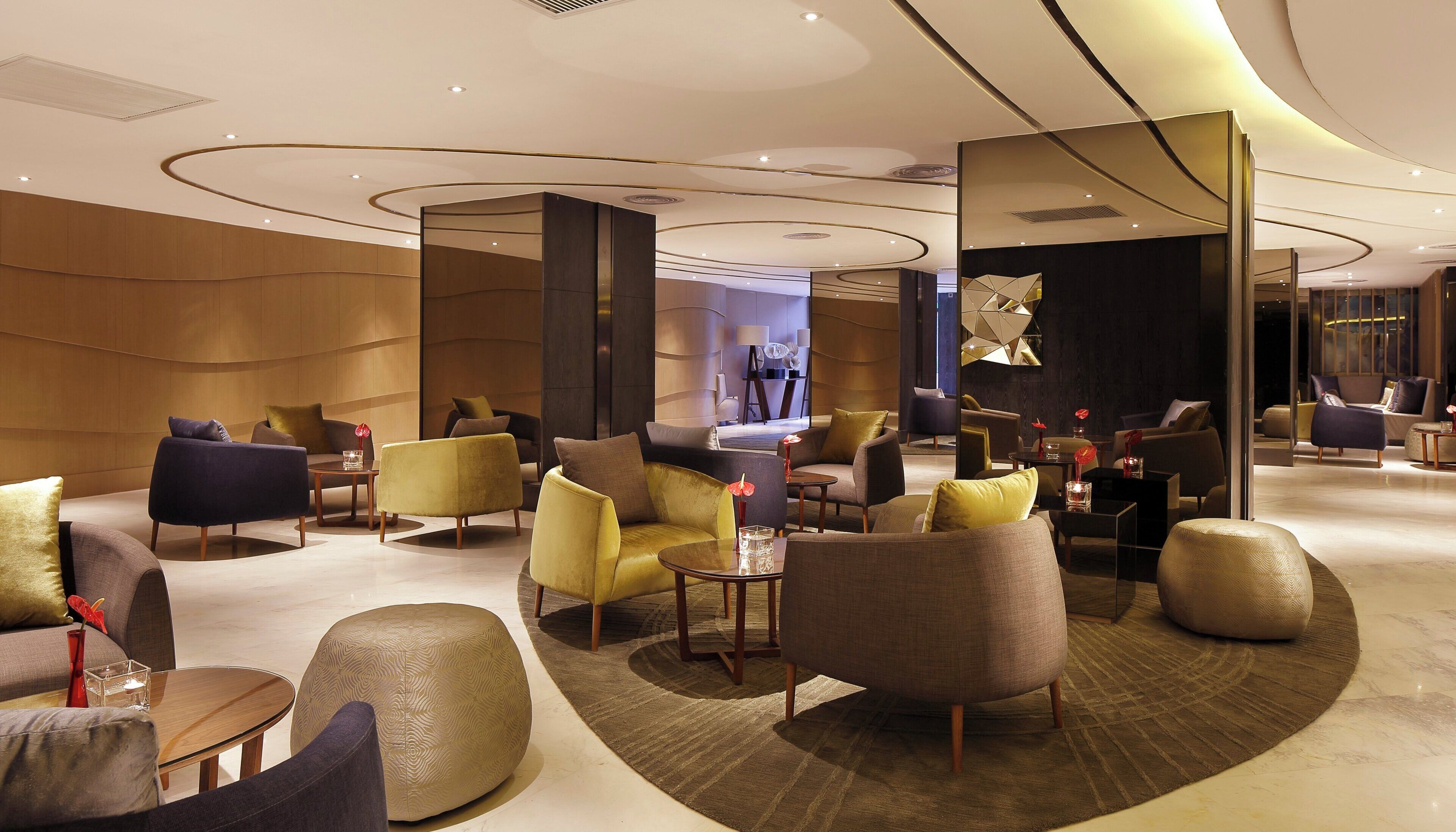 Un moderno hall de hotel con diversas opciones de asiento, incluyendo sofás y sillones, dispuestos alrededor de una zona central con una mesa de centro.