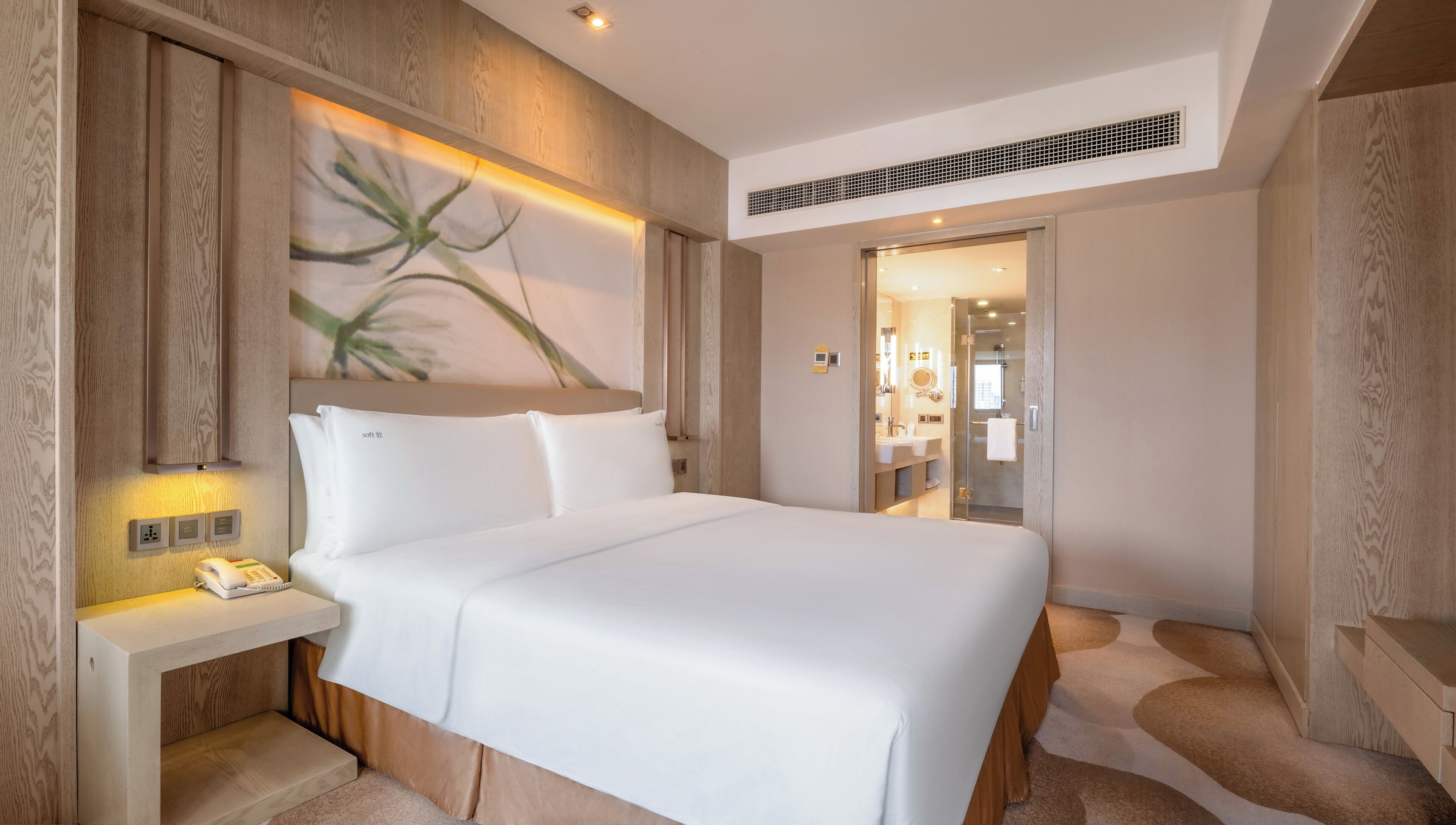 A modern hotel room with a large bed, bedside controls, a telephone, and a painting on the wall.
