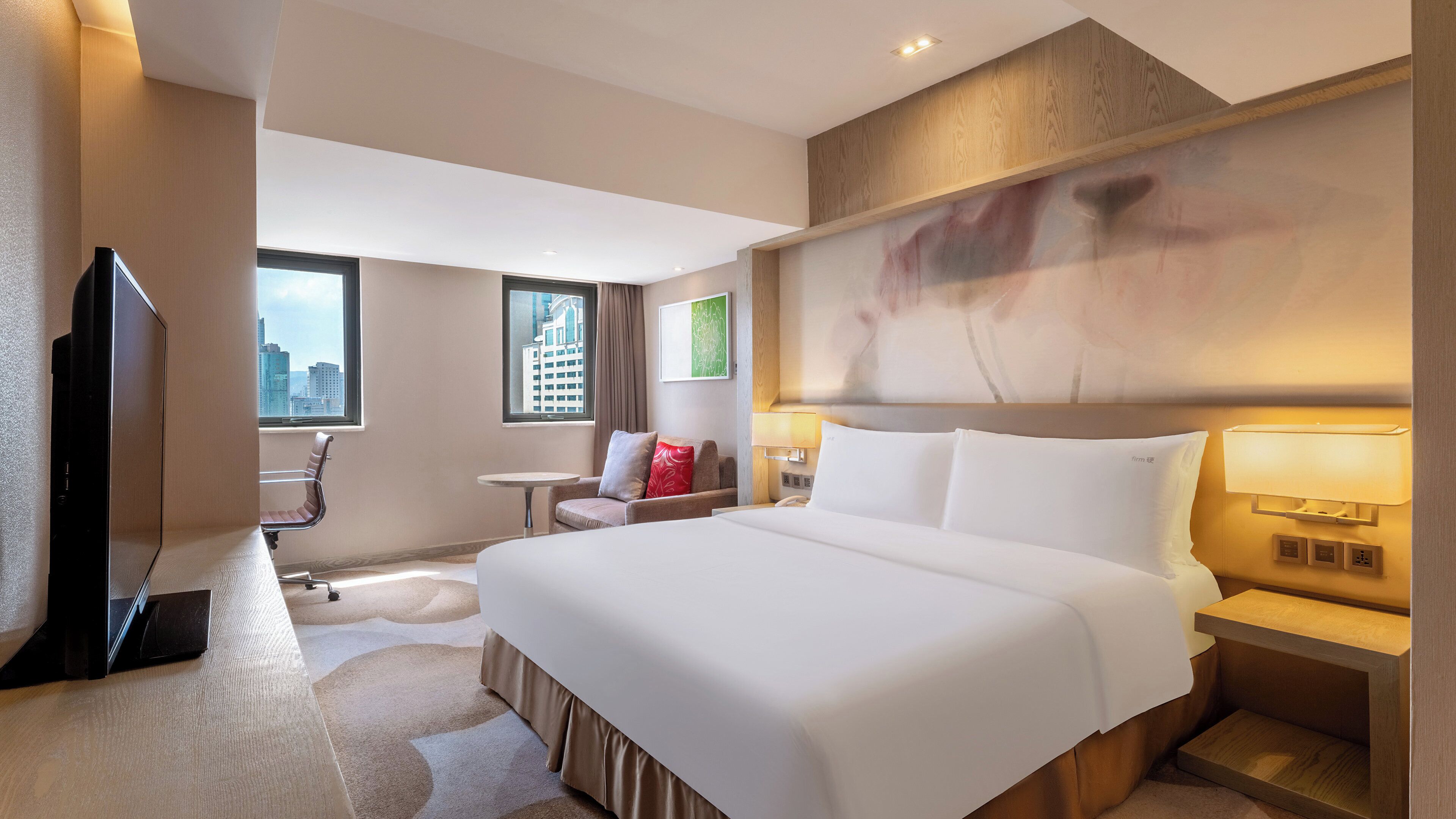 Ein Hotelzimmer mit einem großen Bett, einem Fernseher, einem Schreibtisch und einem Sessel.
