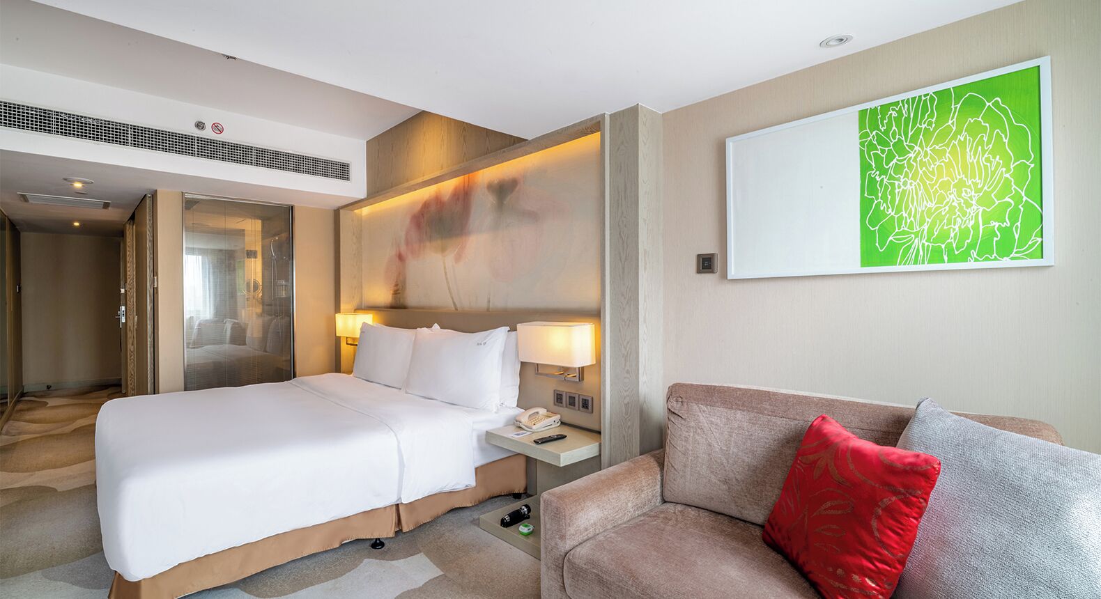 Habitación de hotel con cama, mesita de noche, lámpara, sofá y un cuadro abstracto grande en la pared.