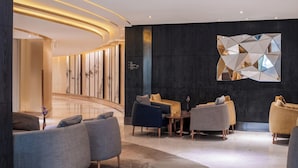 A modern lobby with a curved reception desk, seating area with sofas and armchairs, and a decorative wall piece. - Holiday Inn Kunming City Centre by IHG (Kunming)