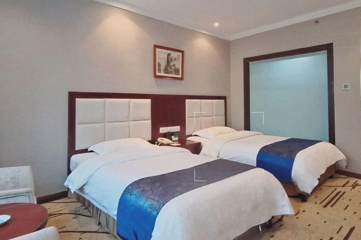 A hotel room with two beds, a bedside table with a phone, and a carpeted floor.