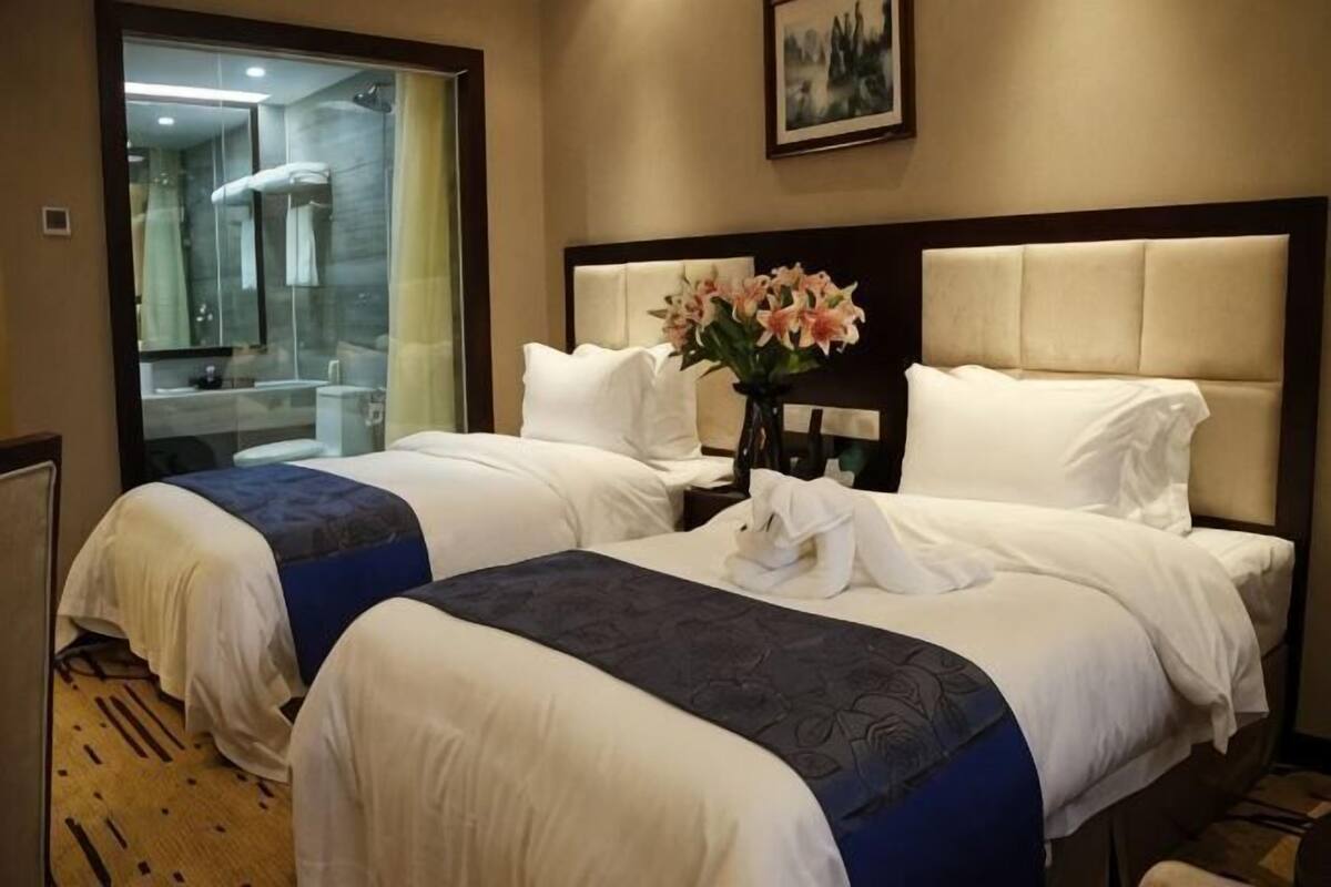 A hotel room with two beds, a bathroom, and a large window.