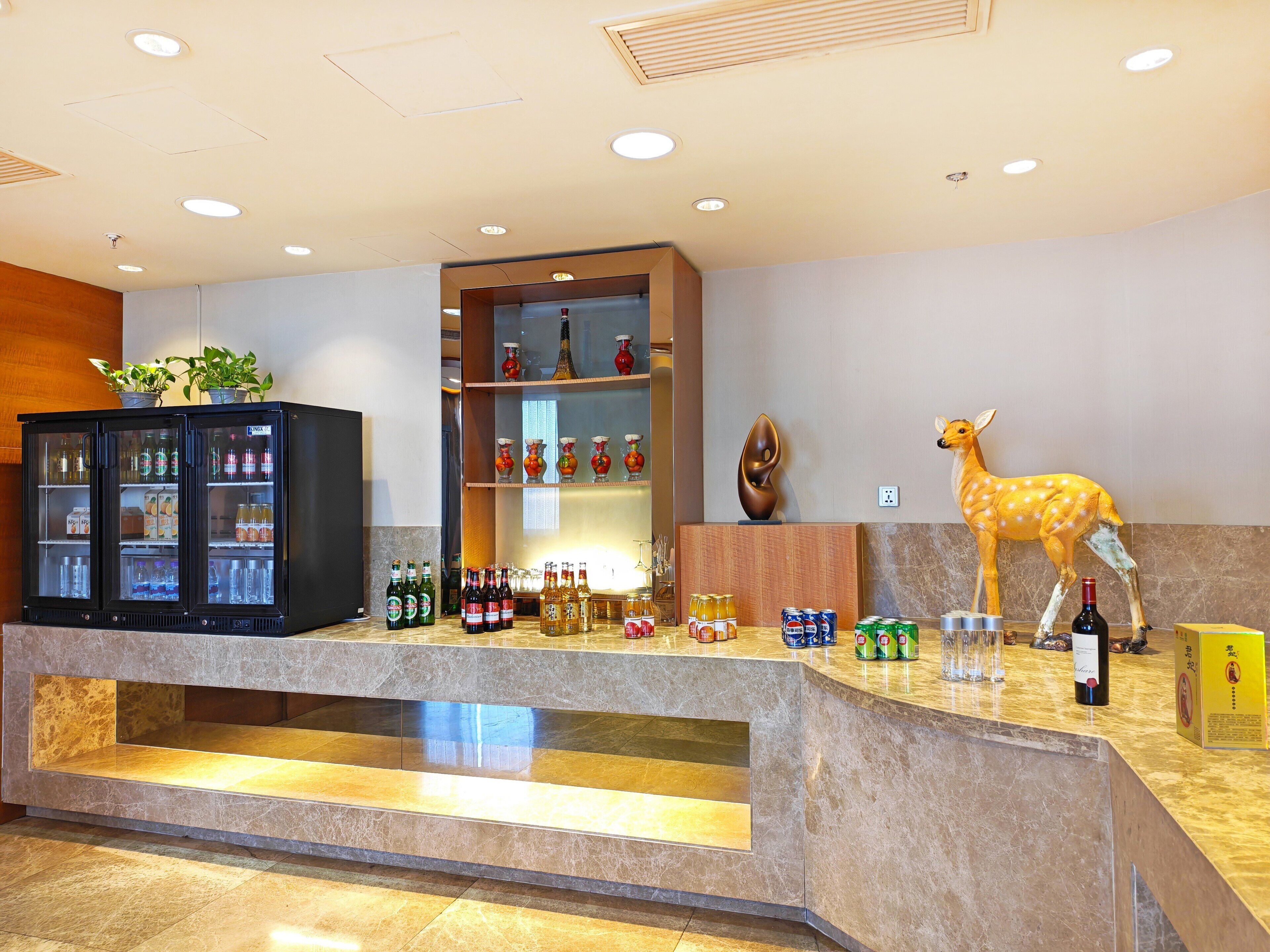 Zona de recepción con mostrador de mármol, refrigerador para bebidas, estantes con botellas y una estatua decorativa de un ciervo.