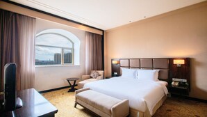 A hotel room with a large bed, a desk, a chair, and a view of the city through a large window. - Holiday Inn Mudanjiang by IHG (Mudanjiang)