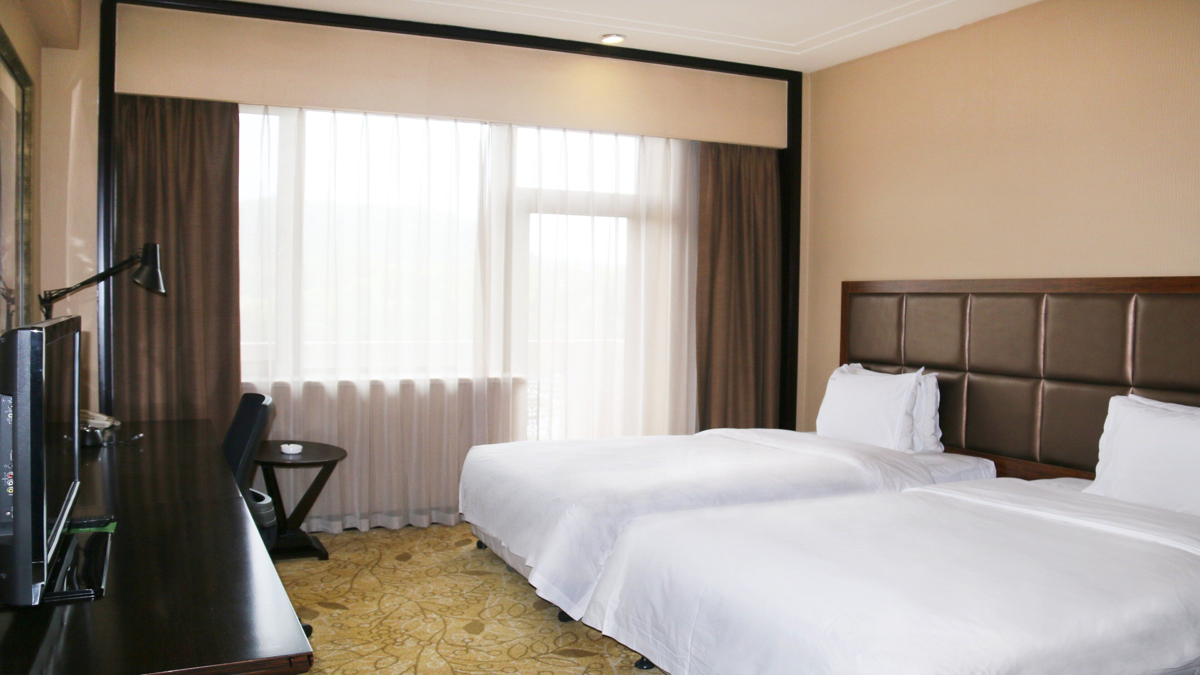 Une chambre d’hôtel avec deux lits, un bureau, une chaise et une petite table.