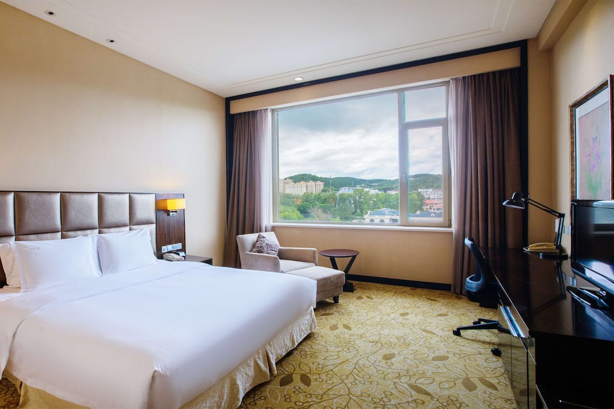 A hotel room with a large bed, a desk with a computer, a chair, and a TV.