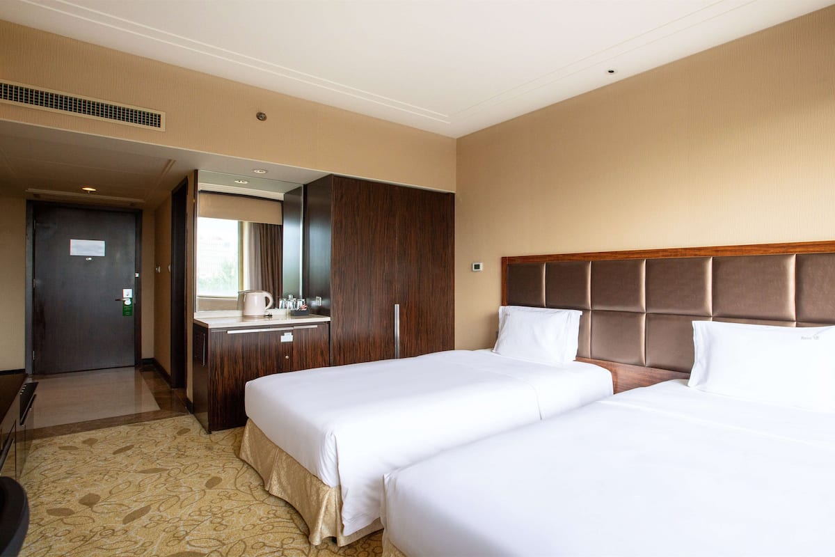 A hotel room with two beds, a desk with a mirror, and a door leading to another room.
