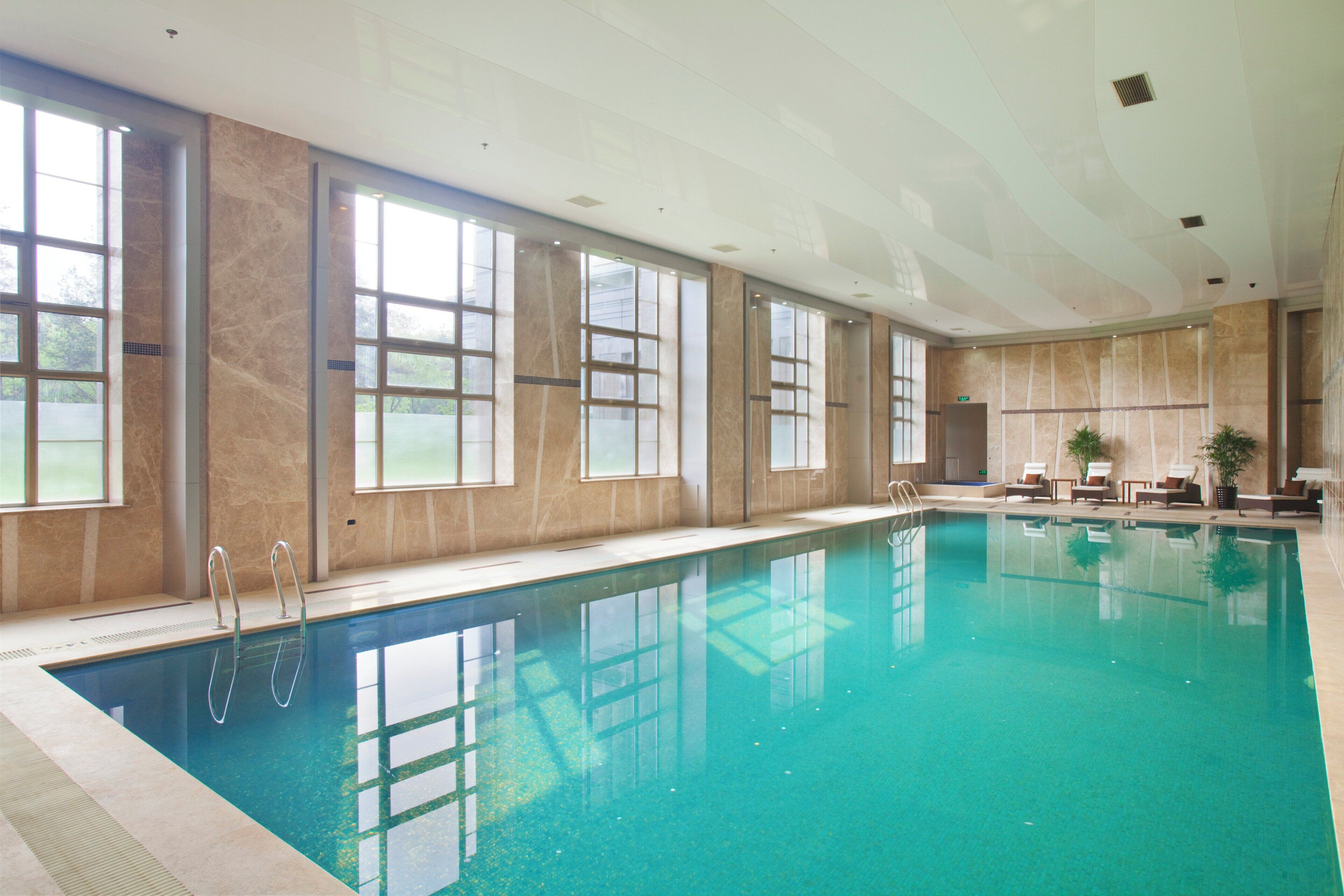 A large indoor swimming pool with clear water, surrounded by large windows and a high ceiling.