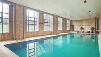 A large indoor swimming pool with clear water, surrounded by large windows and a high ceiling.