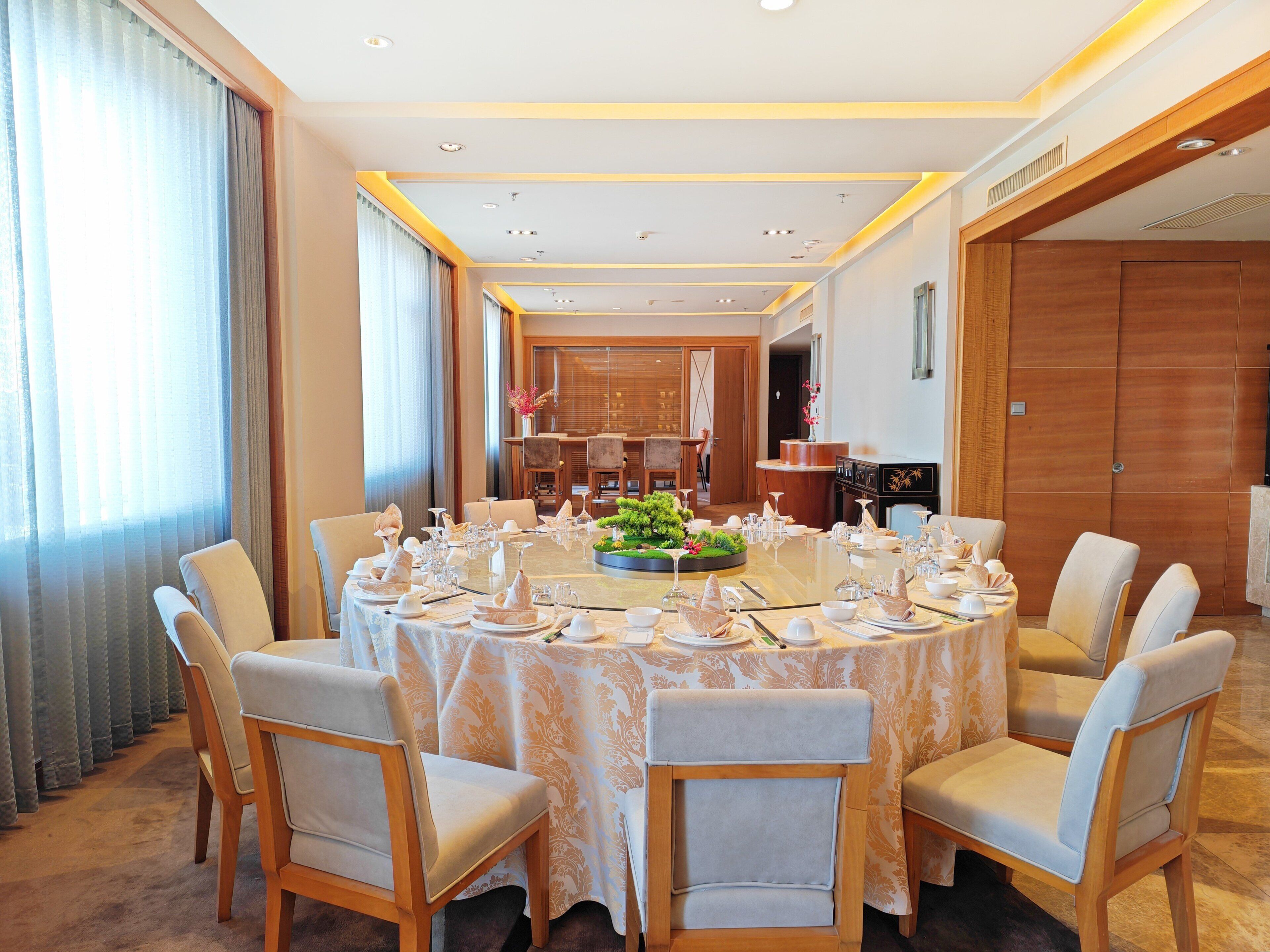 A round dining table with chairs, a chandelier, and a view of a kitchen area.