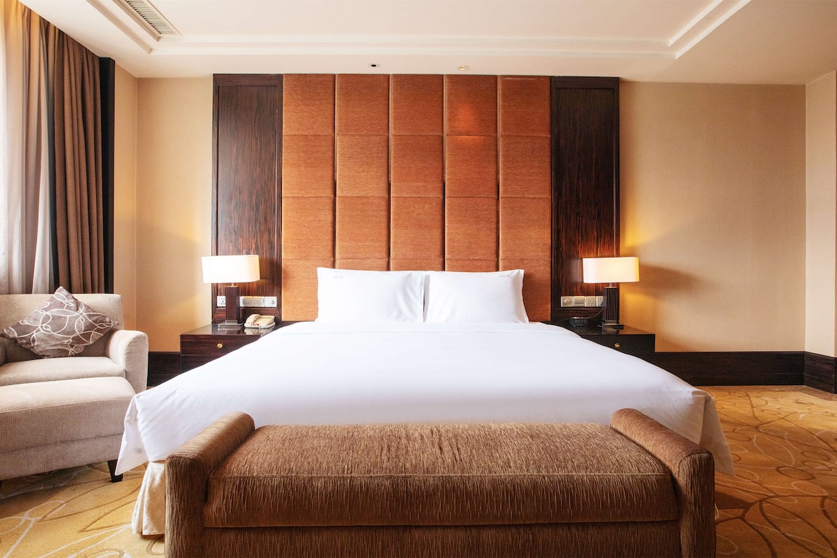 A hotel room with a large bed, two bedside tables with lamps, a chair, and a bench.